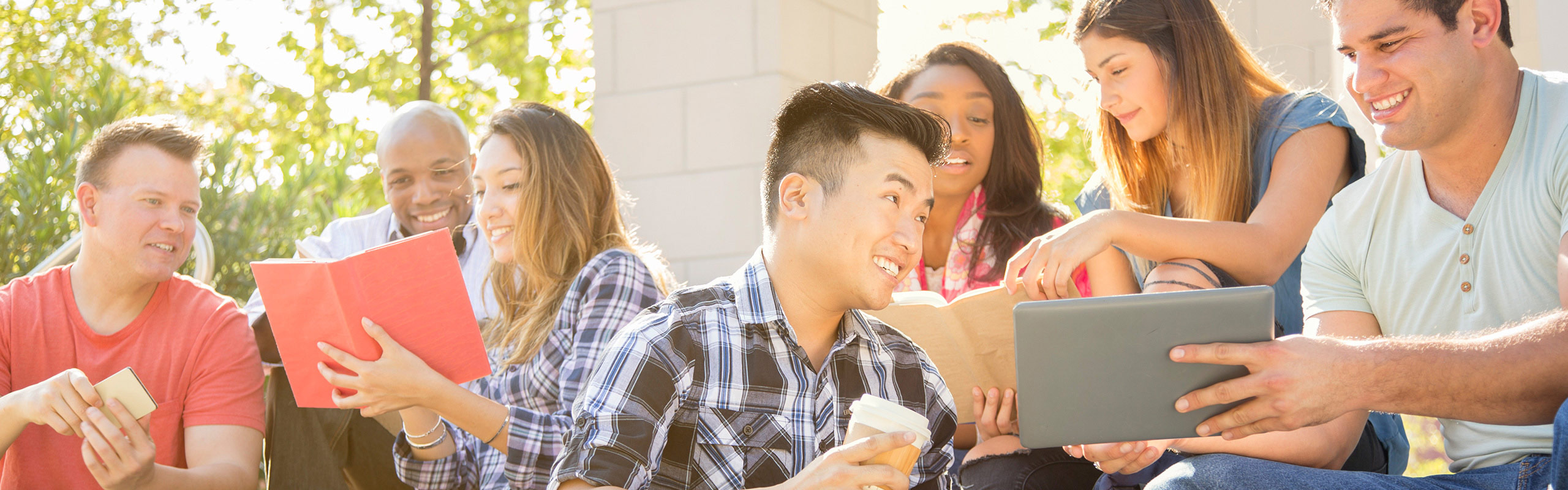 A group of young adult students sitting on the steps of a building, collaborating